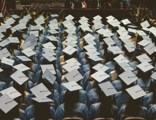 imagem superior de vários formandos vestidos de azul que estão de costas, onde é possível ver com mais destaque seus chapéus de formatura.