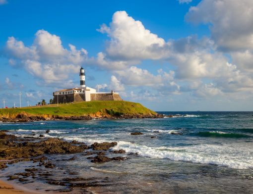 foto de praia em salvador, com mar em ondas pequenas e um farol ao fundo.