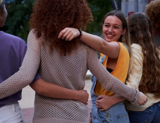 grupo de mulheres de etnias diversas se abraçando em linha enquanto mulher do meio olha para trás