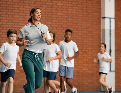 mulher veste roupa de exercício, está fazendo movimentos de corridas e atrás dela vemos crianças diversas como se estivessem correndo também.