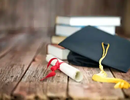 imagem de mesa de madeira com livros empilhados, um diploma e um chapeu de formatura.